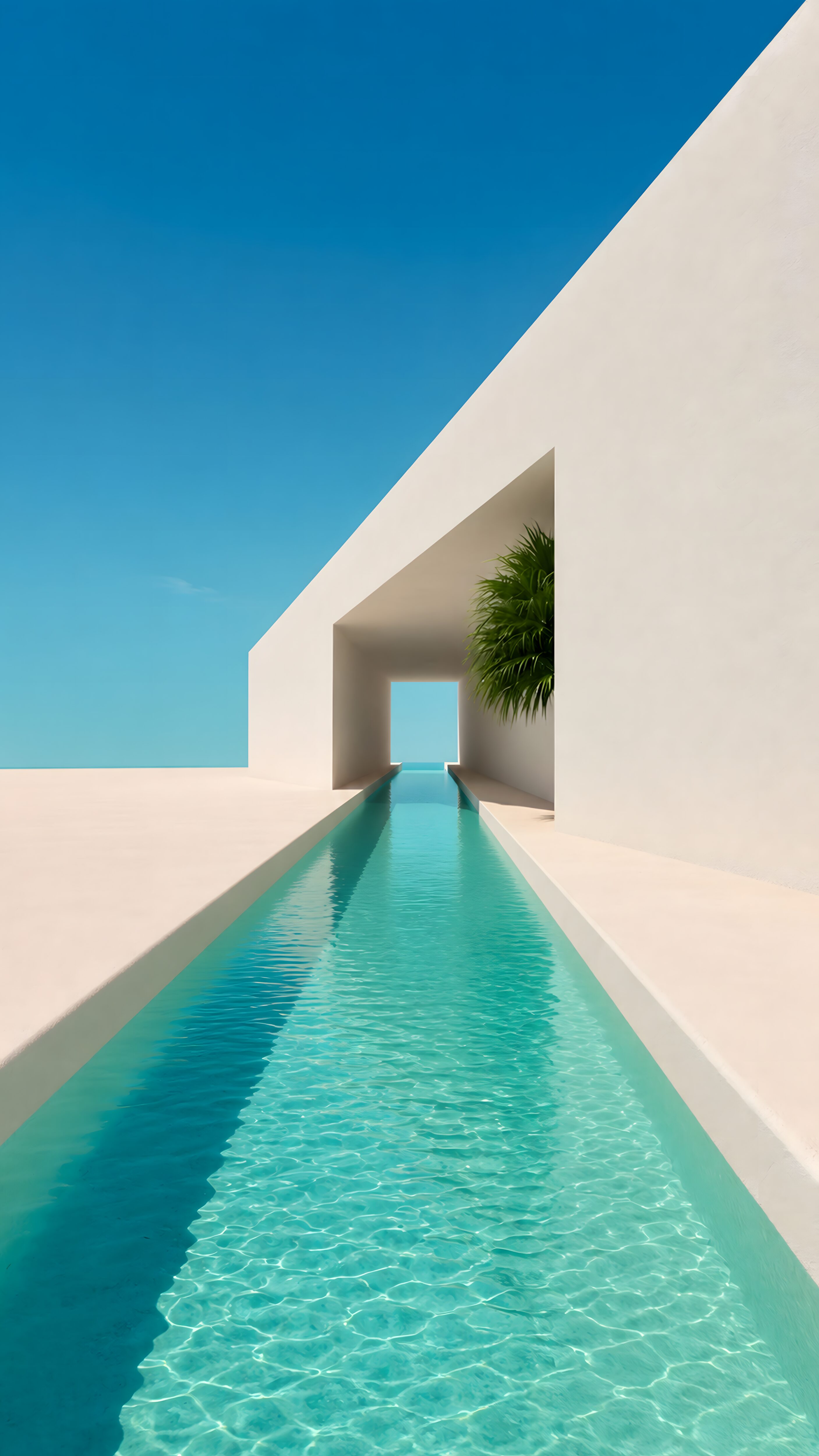 A vertical view of a minimalist white building featuring a long turquoise pool channel leading out to a clear blue sky.